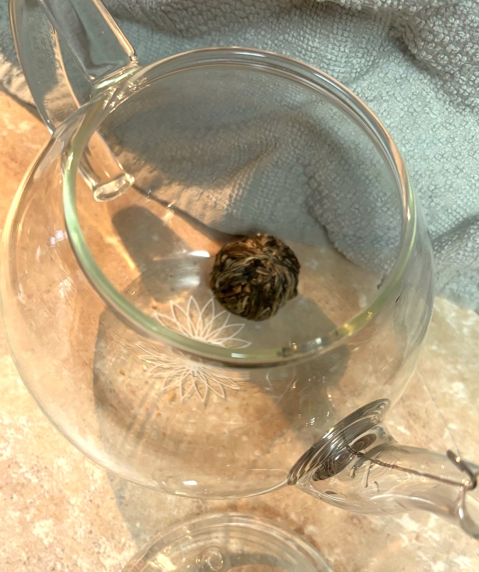 A clear glass tea pod with the lid off reveals from the top view a tea pod sitting inside.